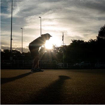 A person is doing lawn bowls with the sun setting behind.