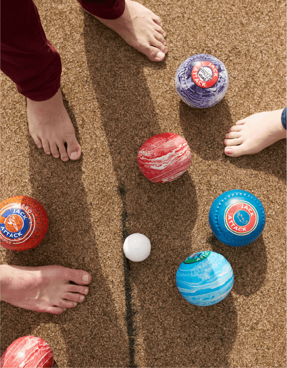 Bare feet gather around a jack and a cluster of lawn bowls on a rink.